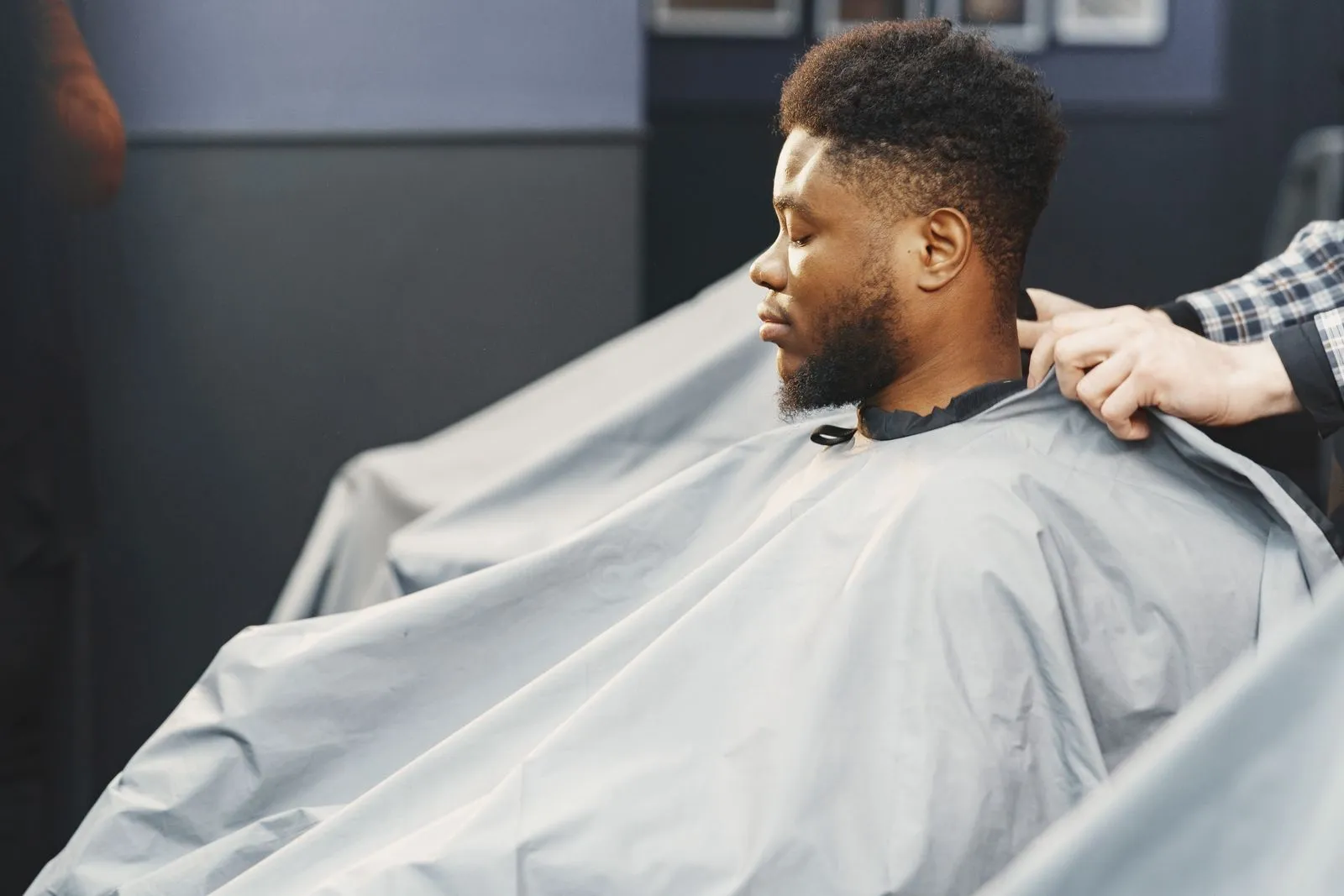A man receives a haircut in a barber shop wearing a protective cape, focusing on grooming.